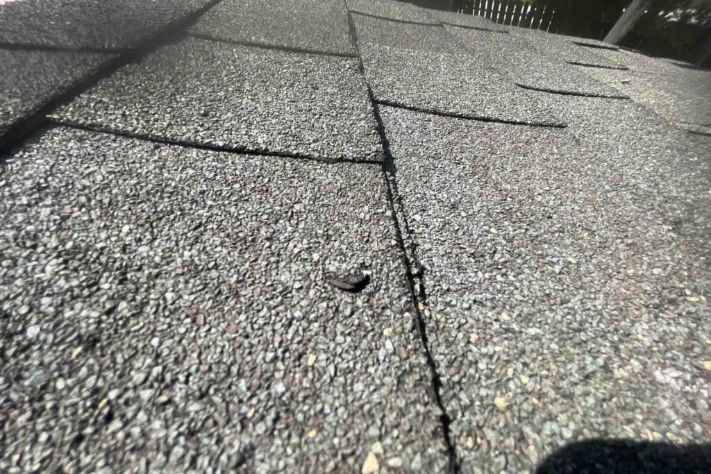 Close-up of a damaged asphalt shingle roof with a visible cracked shingle, illustrating potential repair needs for roof replacement costs in NJ.