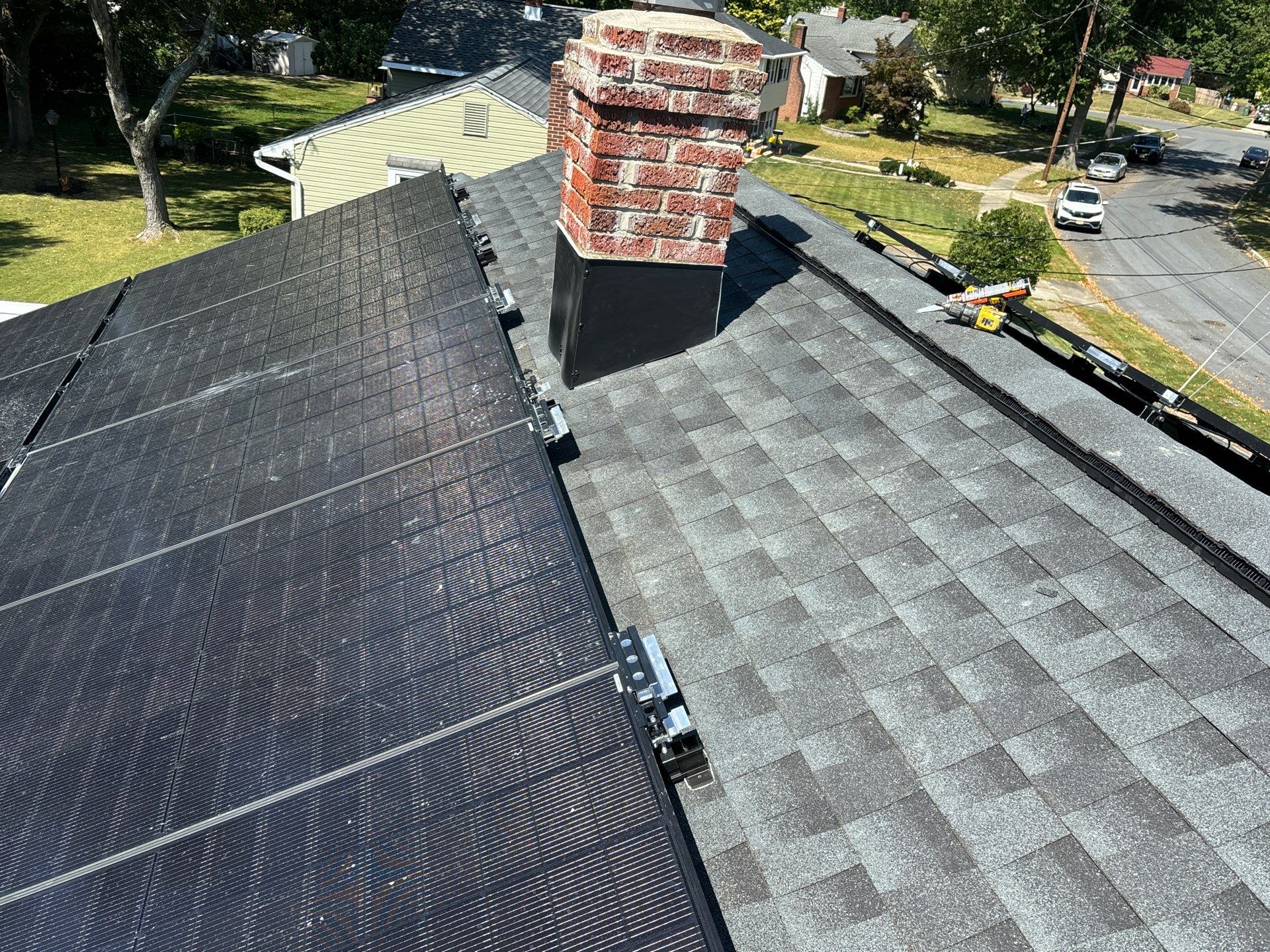 Close-up view of a Cherry Hill roof showing solar panels next to shingled sections and a chimney, illustrating considerations for roof repair vs replacement in Cherry Hill homes.