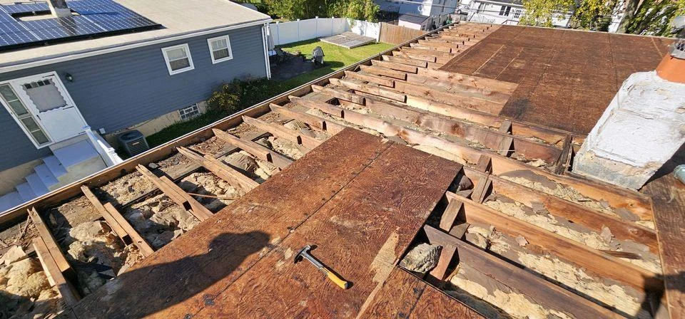 Flat roof under construction, revealing exposed wooden decking and structural elements, highlighting repair needs and factors affecting flat roof installation cost.