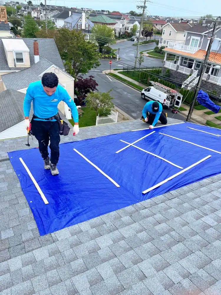 Roofing contractors securing a blue tarp on a residential roof during a storm, providing essential emergency roofing services to prevent further damage.